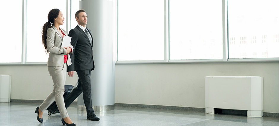 Businesswoman and businessman walking through airport with luggage.
