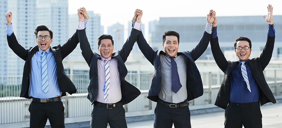 Four happy employees cheering and holding hands on a rooftop.