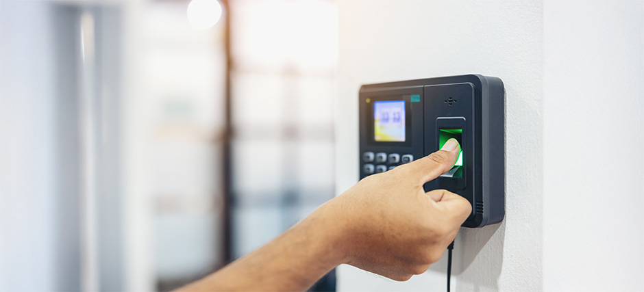 Person pressing finger on biometric fingerprint scanner mounted on wall with screen and buttons visible